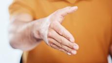 Oranssipaitainen henkilö ojentaa kätensä ja haluaa kätellä ja toivottaa tervetulleeksi. Kuva: Mostphotos.